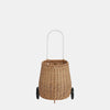 A hand-woven Olli Ella Rattan Luggy with a white handle and black wheels on a white background. The trolley is cylindrical with a woven texture and designed for portability and storage.