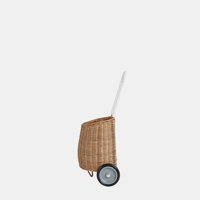 An Olli Ella Rattan Luggy basket on wheels with a metal handle, isolated against a plain, light grey background.