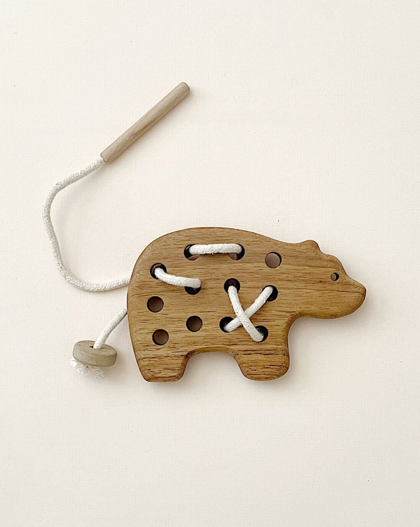 A wooden lacing toy shaped like a bear, designed for developing hand-eye coordination, with holes and a white lace threaded through some of them, against a pale background.