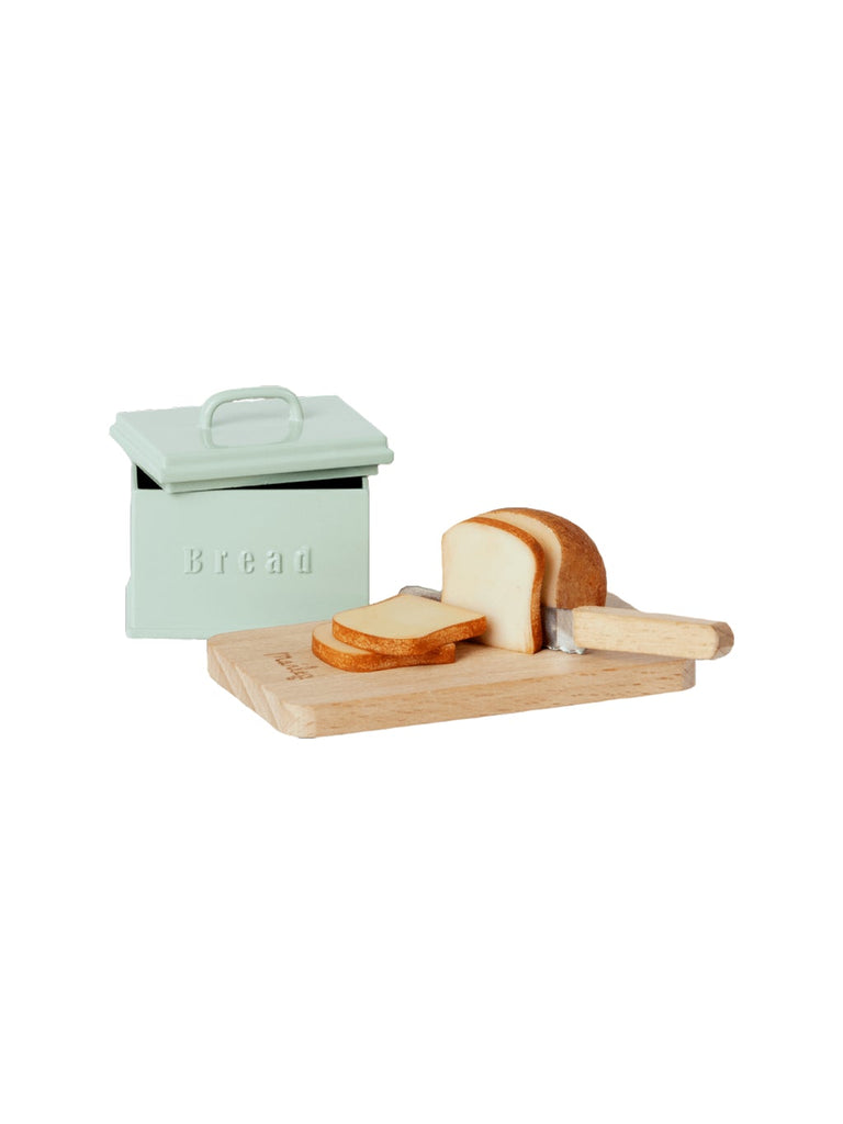 A small rectangular Maileg Miniature Bread Box with a lid labeled "Bread" sits next to a wooden cutting board. This miniature kitchen playset includes a loaf of bread partially sliced, with several slices lying beside the loaf and a knife, creating an adorable hand-painted food scene.