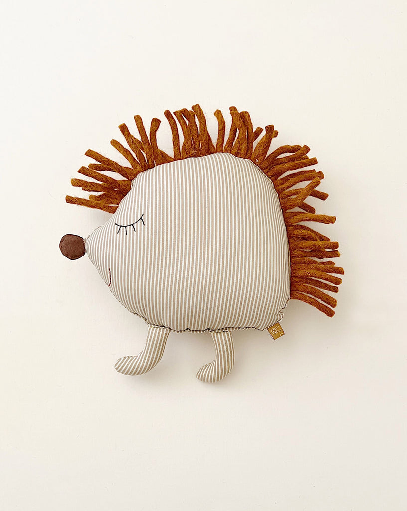 A Hedgehog Cushion with a striped pattern and brown felt spikes, facing left, filled with polyester filling, on a plain white background.