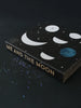 A Me & The Moon – Moon Phase Calendar with a black cover featuring white and blue celestial designs, including a lunar calendar and small stars, against a dark background.