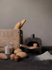 A rustic kitchen scene featuring My Bakery filled with sourdough bread, a cast iron oven, a glass jar, wooden utensils, and bowls, all arranged on a table with scattered flour.
