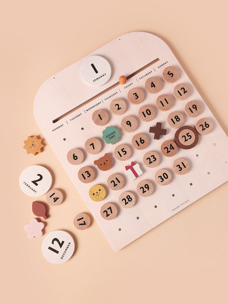 My Calendar is a wooden perpetual calendar with magnetic discs marking days 1 through 31, featuring cute symbols like a leaf and a smiley face, set against a peach background.