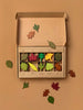 An open cardboard box containing sections of colorful Woodland Leaves shaped like autumn leaves, each labeled with different tree names, scattered on a beige background.