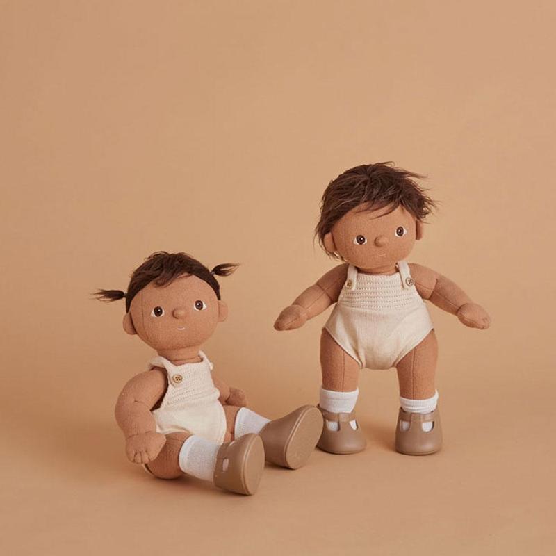 Two Olli Ella Dinkum Dolls with dark hair in cream knit outfits and brown shoes, seated against a plain beige background.
