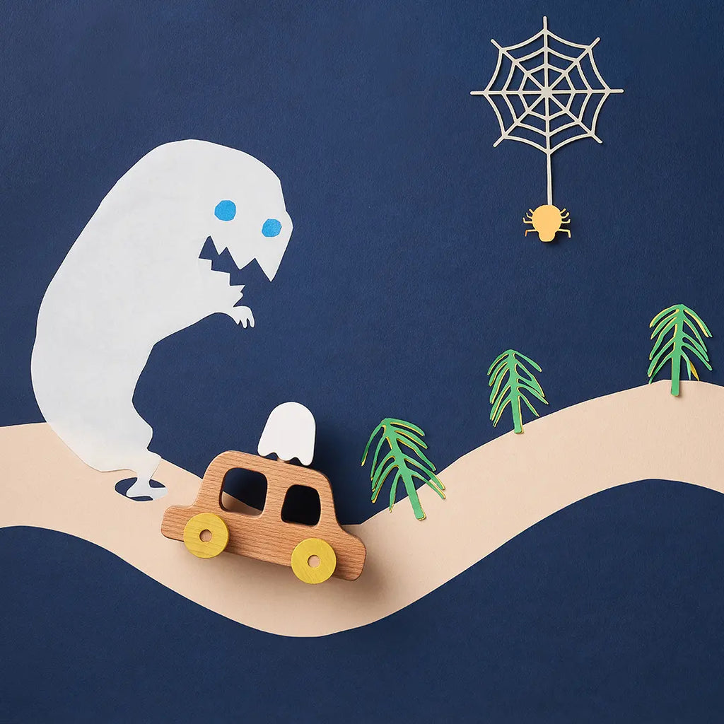 A playful paper art scene featuring a large white monster peeking over a hill, an emotional My Little Car with a ghost, palm trees, and a spider in a web, all set against a blue background