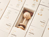 An eco-friendly Nice to Michu Baby Rattle displayed in an open cardboard box, with similar boxes featuring cute character illustrations lined up in the background.