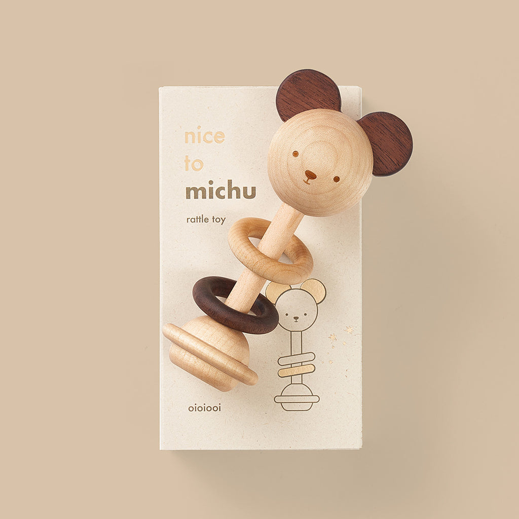 A Nice to Michu Baby Rattle shaped like a bear's head with two rings, displayed on packaging labeled "eco-friendly toy, rattle toy" against a beige background.