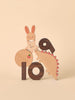 Wooden cutout figures of a rabbit, monster, and the Numbers Play Block Set from Oioiooi on a soft beige background. The rabbit is decorated with a scarf and appears playful, making them