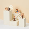 Wooden animal and number blocks displayed on geometric white blocks against a soft beige background. The educational toy set includes a bear, rabbit, and abstract shapes.