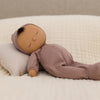 Soft sleeping doll in purple pajamas with brown skin tone. 