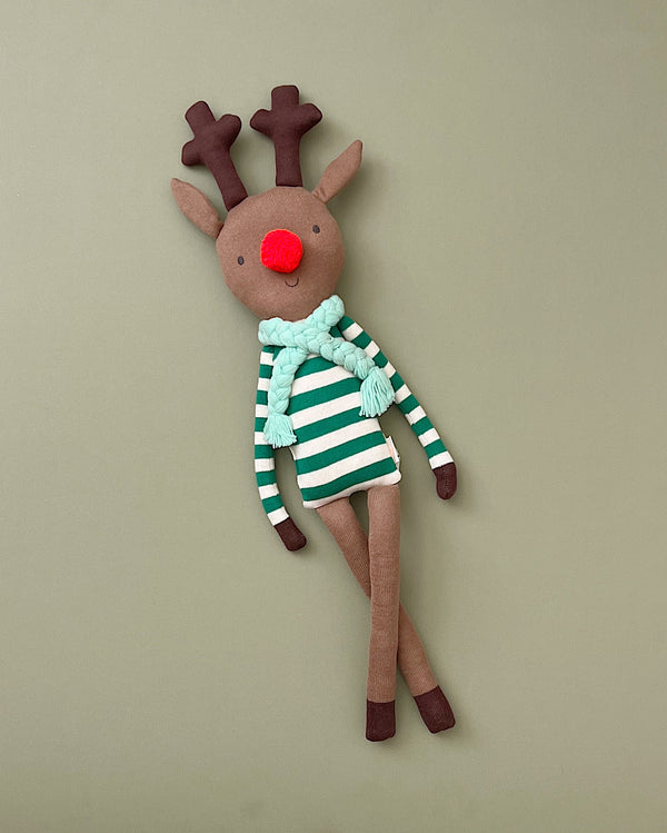 Jingles The Reindeer Toy is a soft, knitted toy featuring brown antlers, a red nose, and a green and white striped shirt. Made from organic cotton, it also sports a light blue scarf around its neck and stands on a plain green background.
