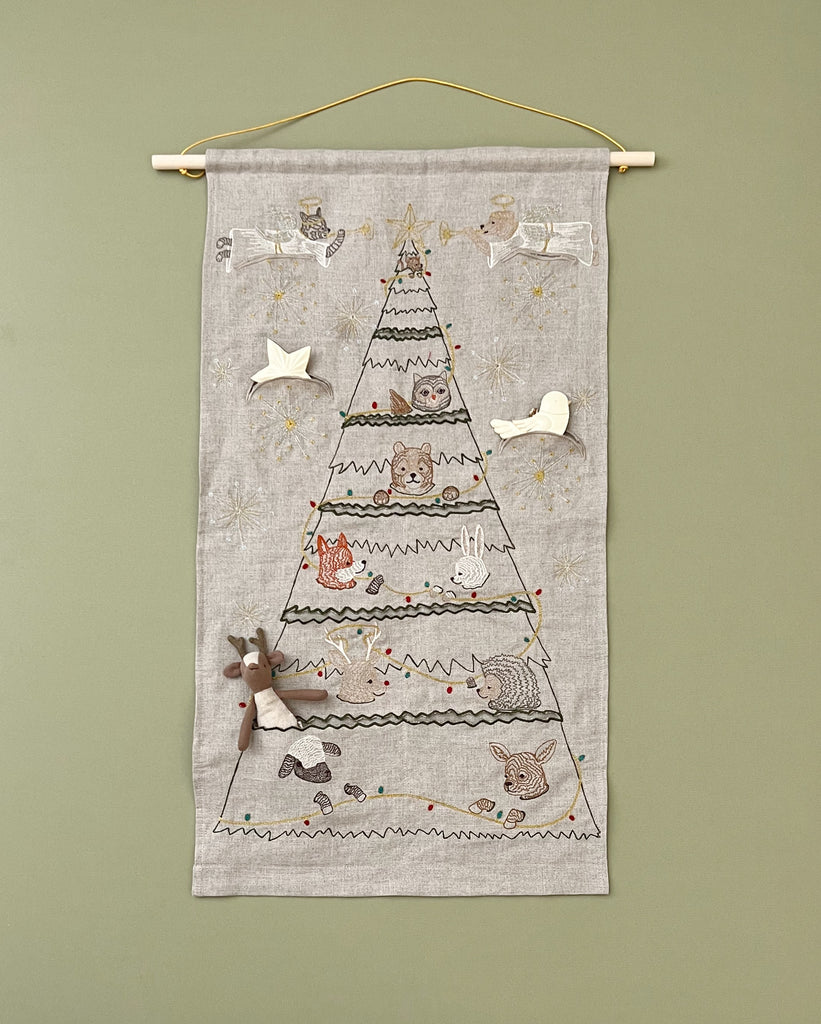 A Coral & Tusk Embroidered Advent Calendar fabric wall hanging featuring a countdown to Christmas design with embroidered animals, stars, and small gifts, hung on a wooden rod against a green wall.