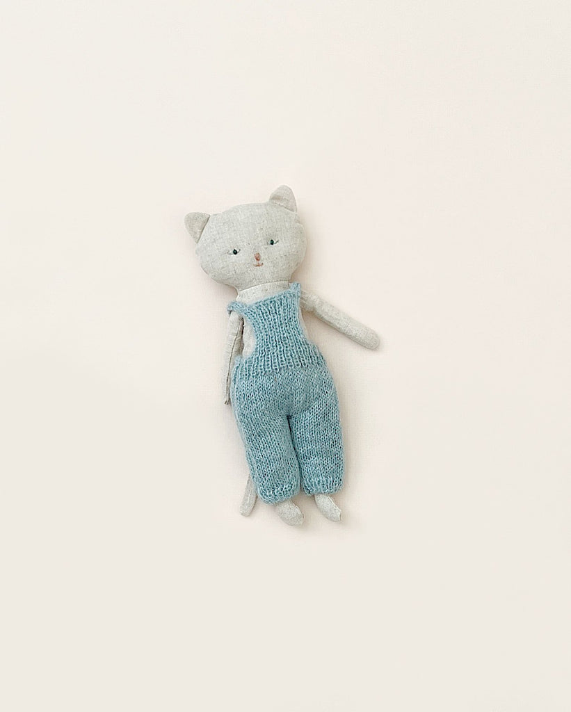 A Maileg Cat Stuffed Animal with a gray head and blue knitted overalls against a plain, light-colored background.