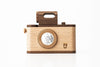 A high-quality Father’s Factory | Vintage Style wooden toy camera with a simple design, featuring a round, faceted lens and a cut-out handle on top, isolated on a white background.