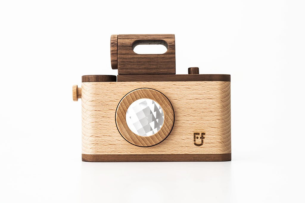A high-quality Father’s Factory | Vintage Style wooden toy camera with a simple design, featuring a round, faceted lens and a cut-out handle on top, isolated on a white background.