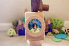 Close-up of a colorful Father’s Factory wooden toy camera with tripod, surrounded by various wooden toy trees and shapes on a carpeted floor.