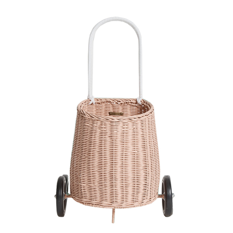 A hand-woven Olli Ella Rattan Luggy shopping trolley with a sturdy handle and two wheels, isolated on a white background.