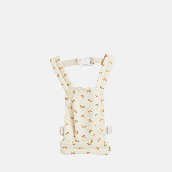 A Olli Ella Doll Carrier featuring a white background adorned with a colorful rainbow pattern, equipped with adjustable straps and buckles, isolated on a plain background.