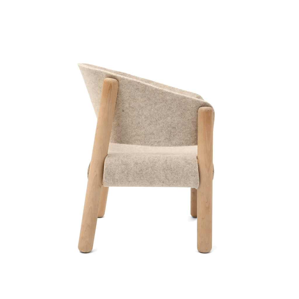 A Charlie Crane SABA Chair 'Fur' with a beige fabric seat and backrest. The chair features a distinctive raw beech wood frame with four legs and a slightly reclined back. Its minimalist design blends natural wood and soft upholstery, viewed from a slight side angle.
