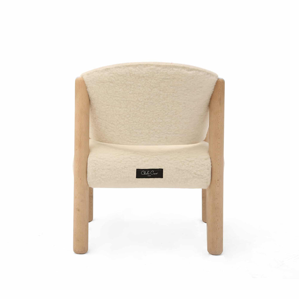 A beige upholstered Charlie Crane SABA Chair 'Fur' with raw beech wood legs, shown from the back. The chair has a soft texture, and a small black tag is attached to the fabric on the lower backrest. The chair is positioned against a plain white background.