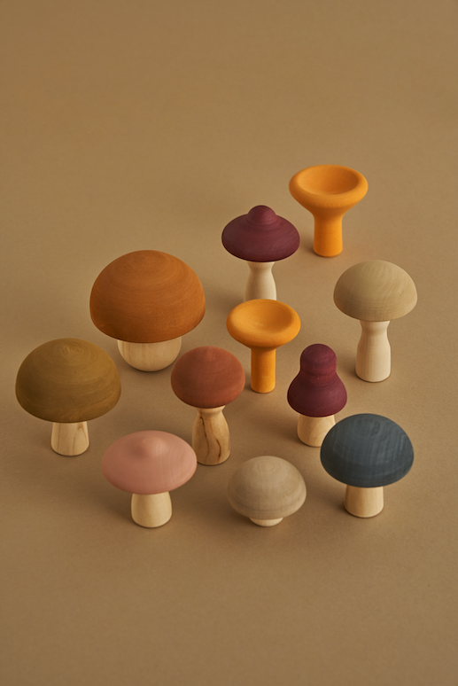 A collection of Raduga Grez Handmade Wooden Mushrooms in various sizes and colors, arranged on a beige background, creating an artistic display of natural tones.
