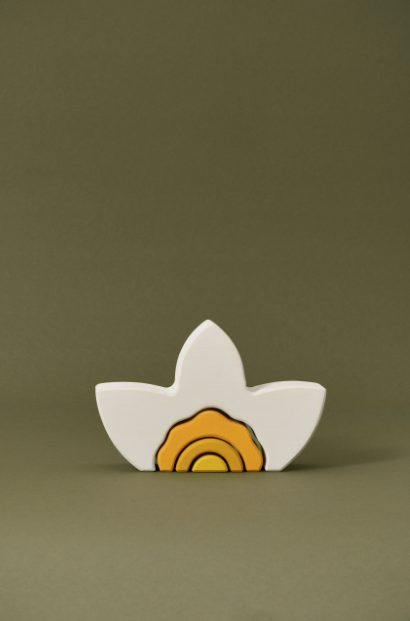 A Raduga Grez Arch Stacker - Narcissus Flower resembling a stylized white bird with yellow and orange body detail, placed against a plain green background.