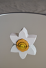 A Raduga Grez Arch Stacker - Narcissus Flower placed on a round mirror reflecting its image, set against a gray background, crafted by Raduga Grez.