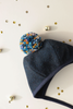 A dark blue wool Briar Baby Eon Pom Bonnet with a colorful pom-pom on top, displayed on a light surface scattered with small gold bells.