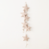 A vertical line of six Handmade Star Garland hanging against a plain white wall, connected by a thin string, creating a simple and elegant handmade decor.