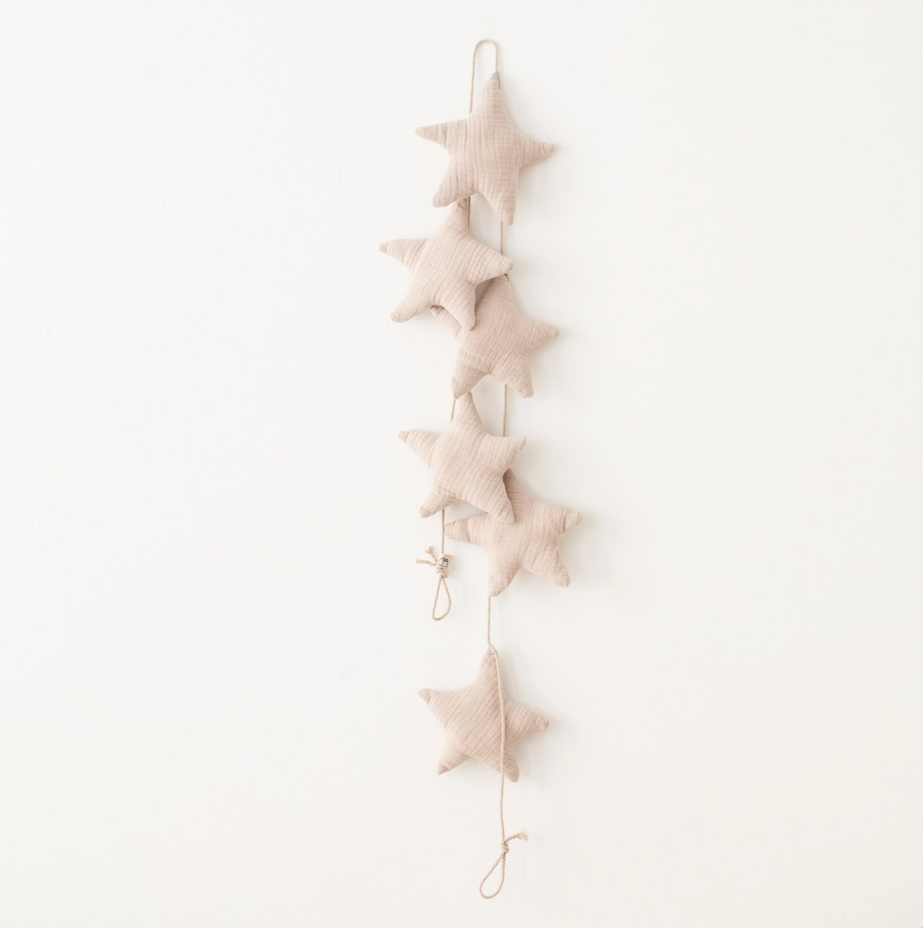 A vertical line of six Handmade Star Garland hanging against a plain white wall, connected by a thin string, creating a simple and elegant handmade decor.
