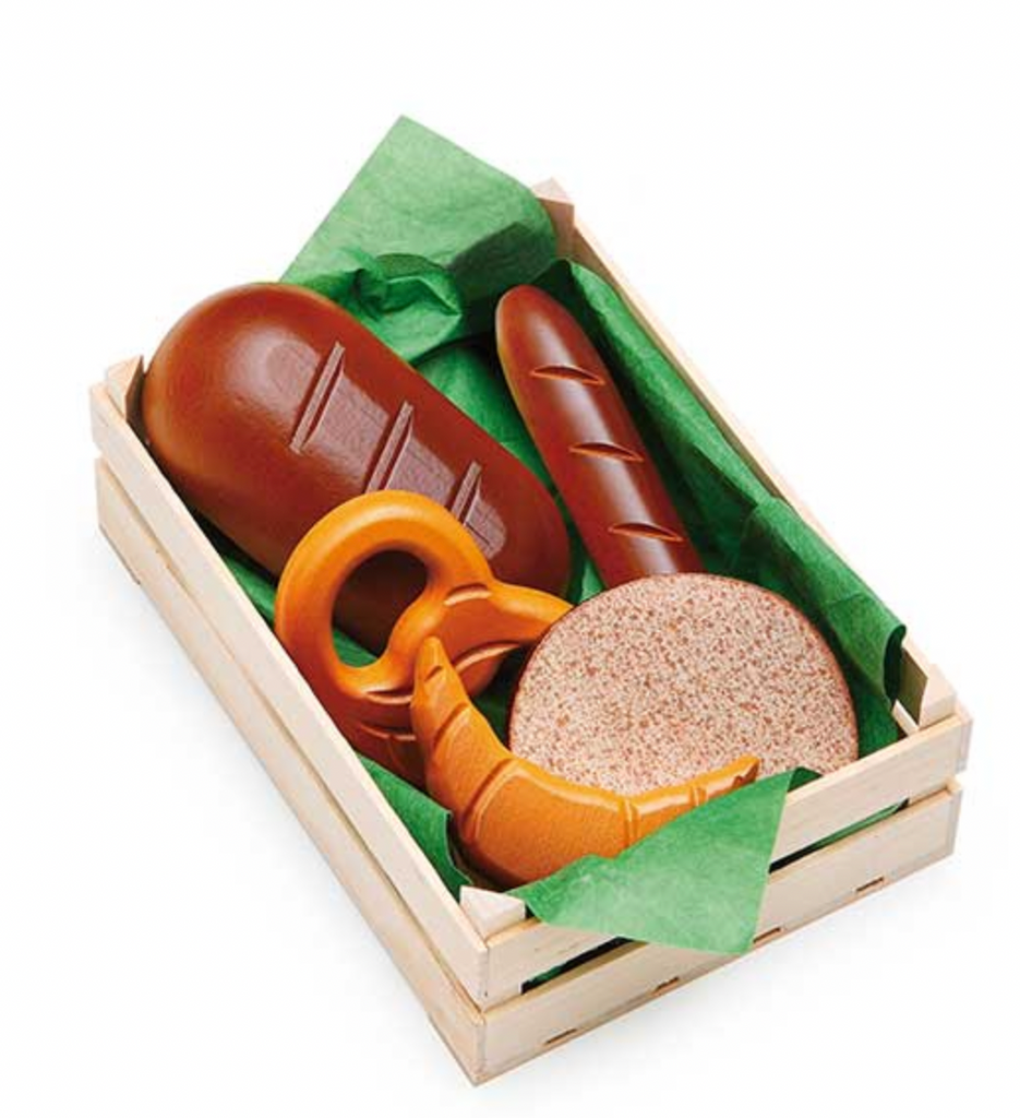 A wooden Erzi gift box containing Erzi Assorted Baked Goods in Crate including a sausage, a pretzel, a loaf of bread, and a round cheese, all nestled on green tissue paper, isolated on.