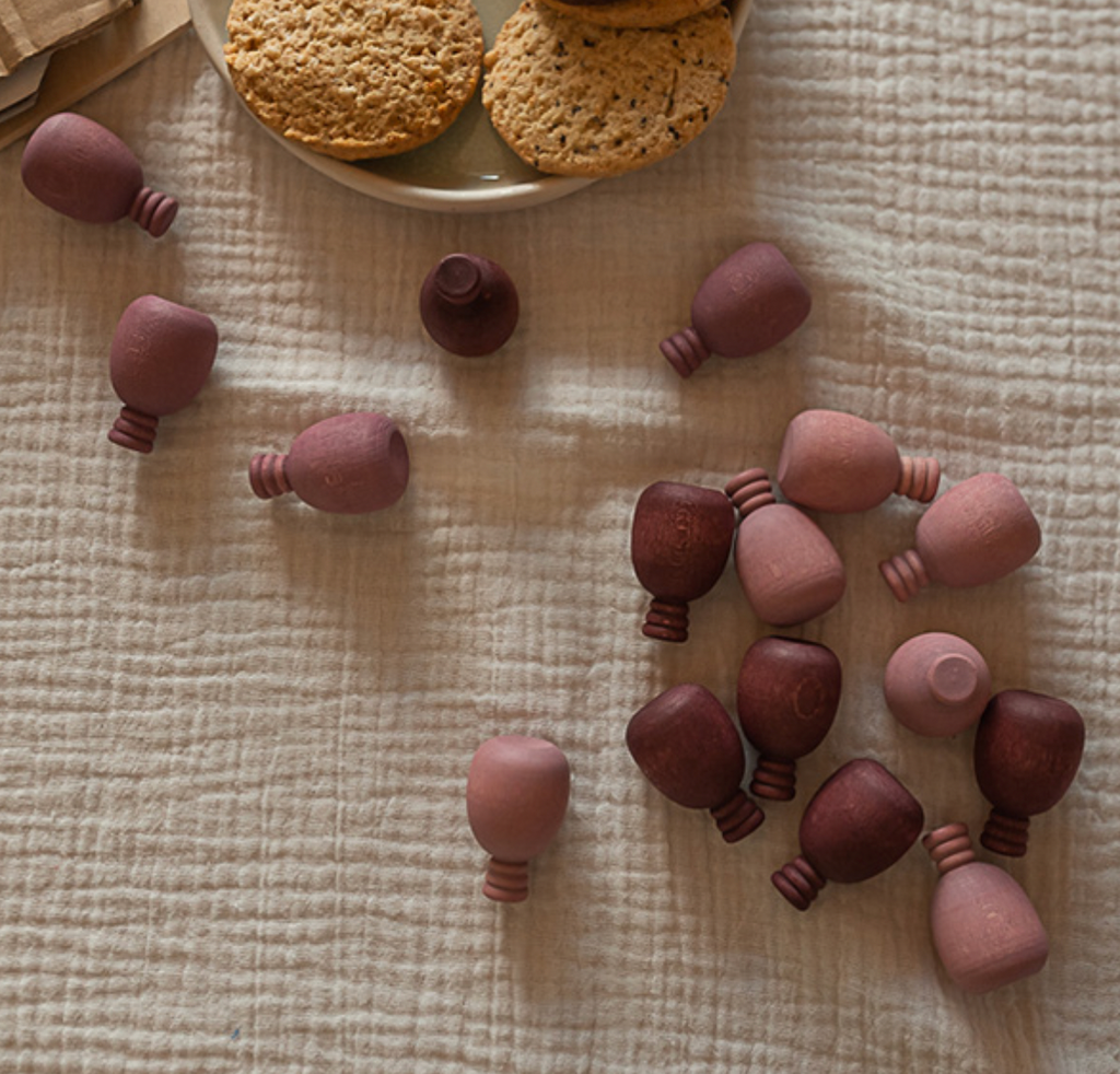 An arrangement of small, wooden barrel-shaped beads scattered on a textured beige surface, accompanied by a plate with Grapat Mandala Pineapples. Subtle warm tones and rustic vibes.