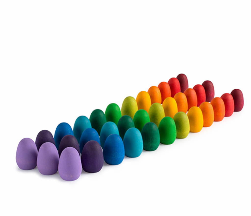 A row of colorful Grapat Mandala Rainbow Eggs made from wood sourced from sustainable forests, arranged in a gradient from purple to red on a white background.
