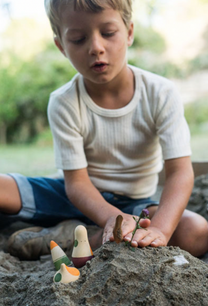 A young boy playing with the Grapat Ooh-la la! Play Set in a sandbox, focusing intently as he positions them on a small mound of sand.