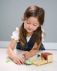 A young girl with long brown hair plays with a Tender Leaf dolls house and a Tortoise Pet Set on a table, looking focused and content.