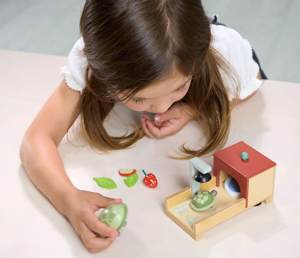 A young girl plays with a Tortoise Pet Set dolls house that includes cozy home accessories and a toy cabbage in her hand.