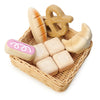 A collection of wooden toy food items including bread, pretzel, and marshmallows, arranged in a handcrafted Market Basket on a white background.