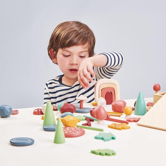 A young child engages in open-ended play with My Forest Floor, concentrating on stacking a piece. The background is light grey.