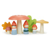 A whimsical scene featuring wooden figurines of the Woodland Gnome Family with red hats, two large mushrooms, and colorful leaf shapes in the background. The gnomes are painted in different outfits, and the overall scene has a playful, handcrafted feel reminiscent of Merrywood Tales.