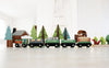 A Wild Pines Train Set carrying various timber trails playset figures, including trees, a house, and an animal, on a bright, simple indoor setting with a white background.