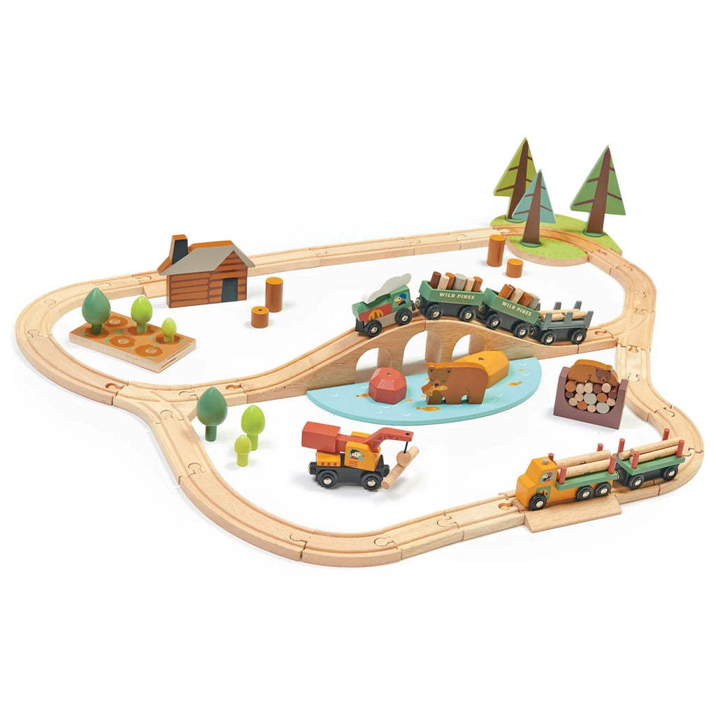 A Wild Pines Train Set featuring tracks forming an oval shape with a bridge, trees, a cabin, logging truck toy, a lake, and a toy train carrying various items.