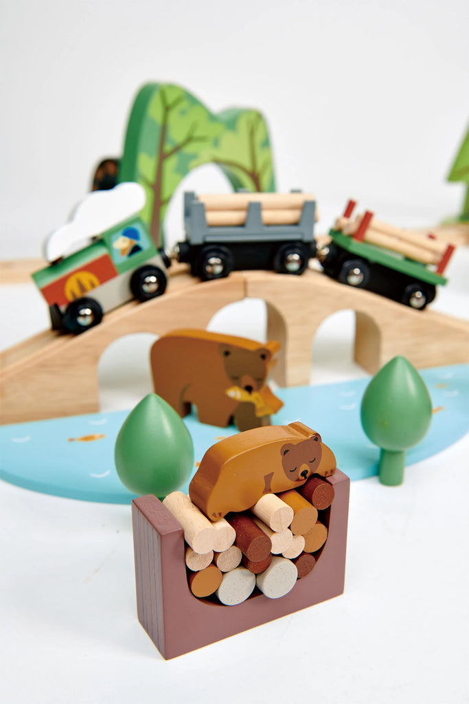 A colorful wooden Wild Pines Train Set featuring animals, trees, and various vehicles like a car, logging truck, and train on a play mat with roads and scenery.