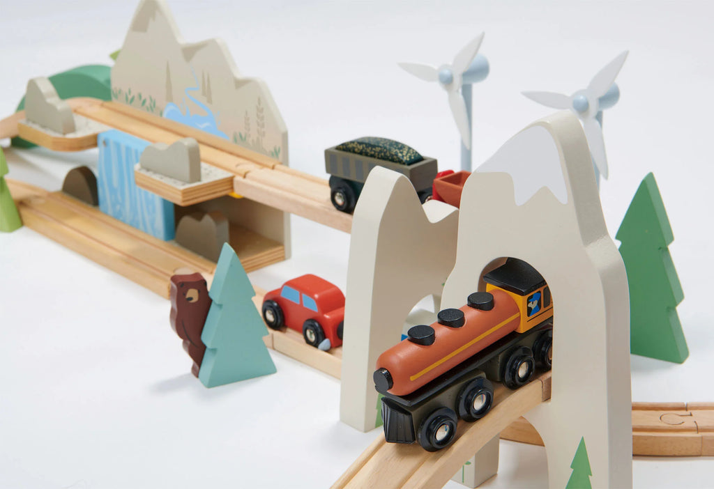 A colorful Mountain View Train set featuring a train on a bridge, mountains, trees, cars, and wind turbines on a clean, white background.