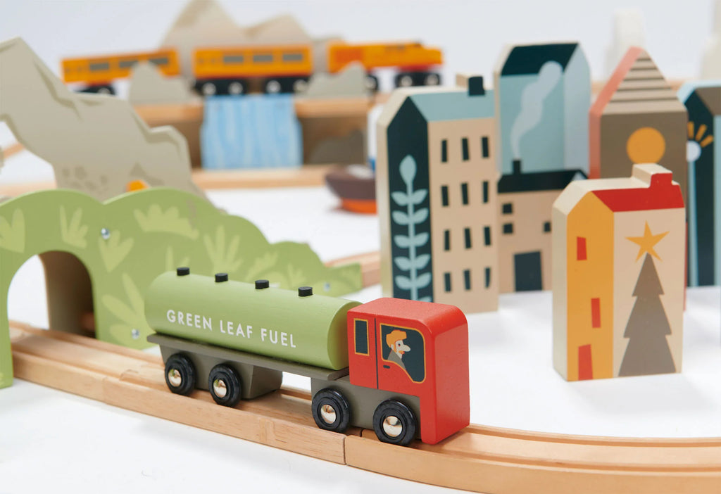 A colorful wooden toy train labeled "Mountain View Train set" on a track, with various wooden buildings and trees in the background, resembling a vibrant small town.