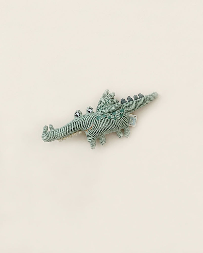 Sentence with product name: A Baby Crocodile Rattle, displayed on a plain, light beige background. This toy is made of 100% cotton.