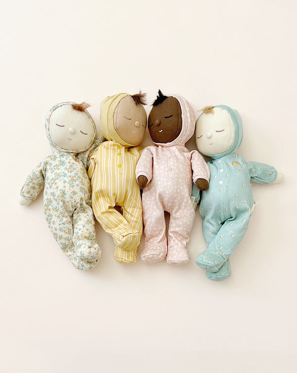 Four Olli Ella Dozy Dinkum Dolls in floral, striped, and polka-dotted 100% cotton onesies, lying side by side against a light background.