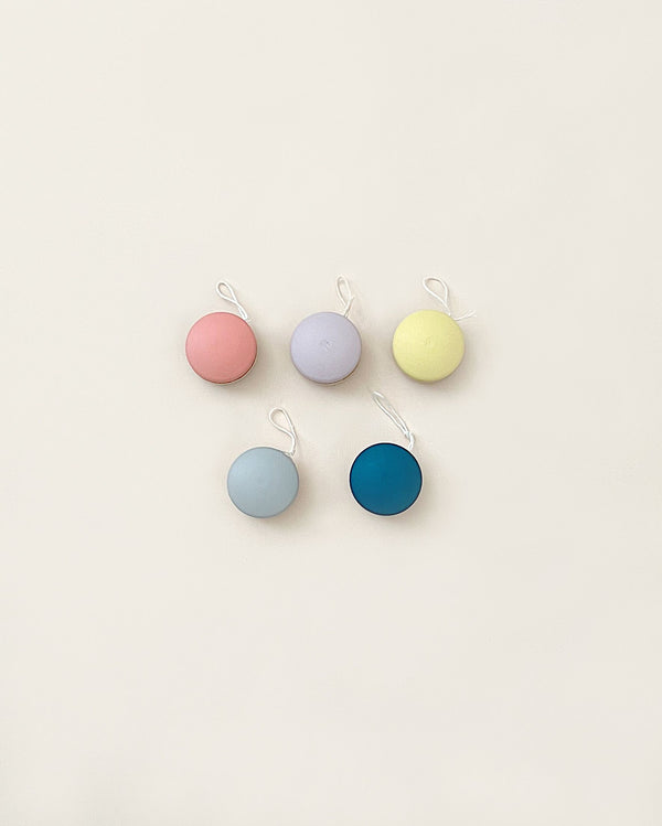 Six colorful round tags in pink, purple, yellow, light blue, teal, and dark blue, neatly arranged in two rows against a light beige background. They are Wooden Yoyo size.