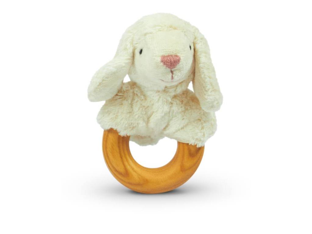 A Senger Naturwelt Sheep Teether with a soft white plush lamb head attached to a cherry wood teether. The lamb has droopy ears, a pink nose, and stitched black eyes. Handmade in Germany, the rattle is photographed against a white background.